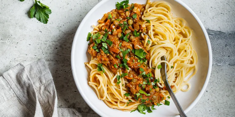 vegane Sauce Bolognese mit Spaghetti serviert in einem weißen Teller auf einer Marmorplatte<br/>